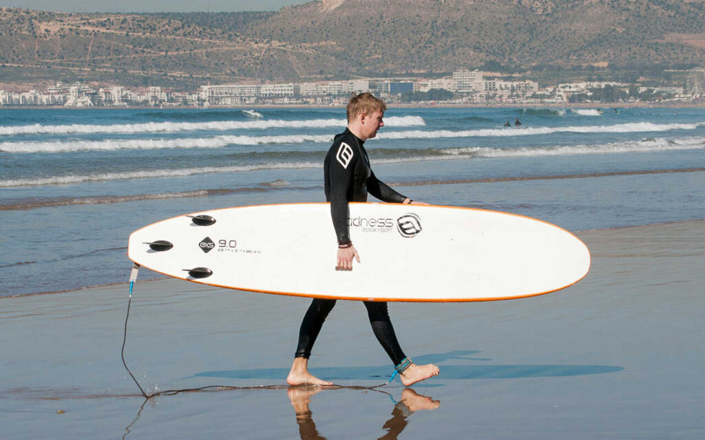 guy in a wetsuit walking on the beach with a softtop surfboard