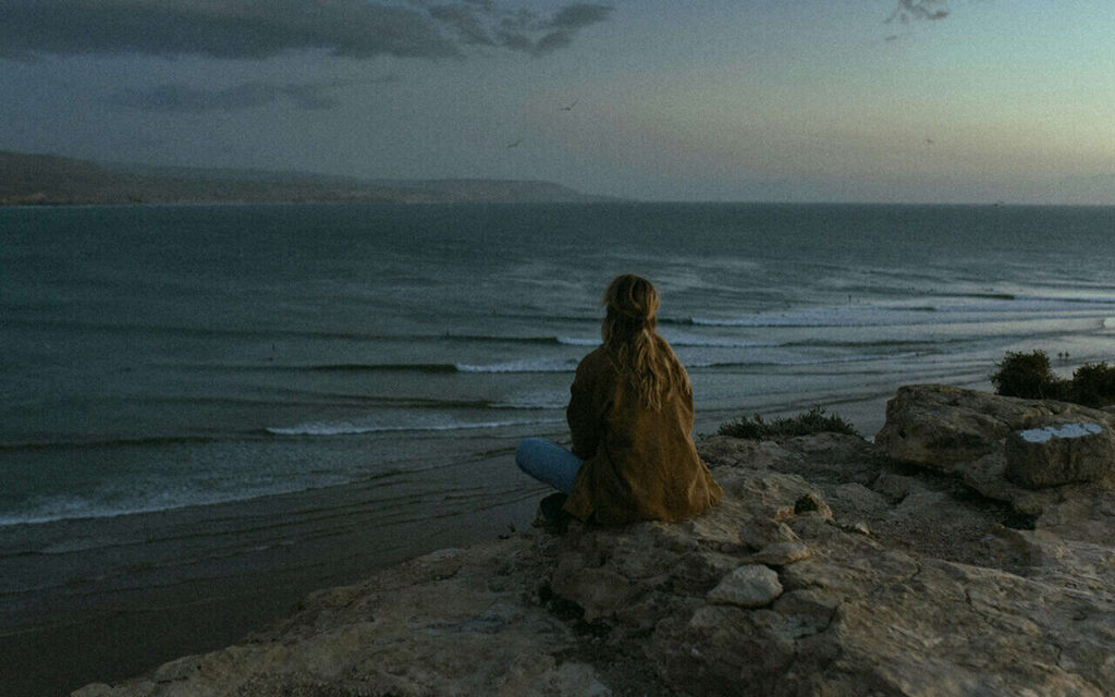 surfer girl sitting on a rock watching the ocean imsouane morocco