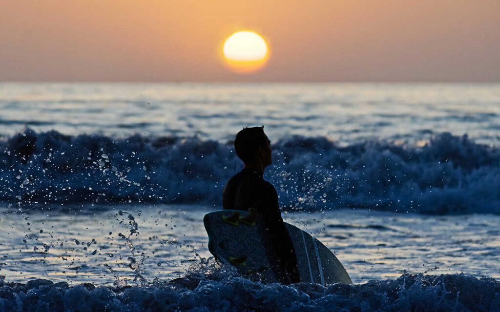 surfer walking into the waves on the sunset holding a shortboard